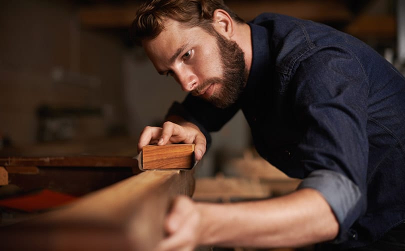 who-we-are-focus-kerioth man with a beard hand sanding a fine piece of wood